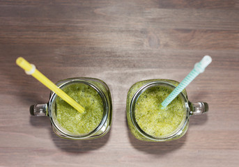 Two green smoothies in a mason jars with tubes on wooden background