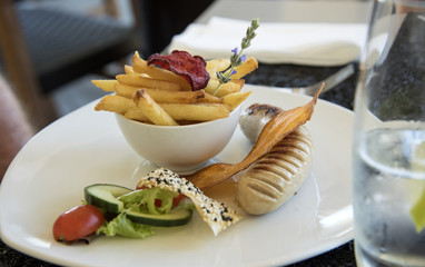 A child's meal of upmarket sausage and a bowl of chips with a small salad