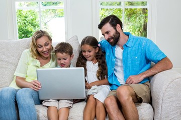 Smiling children with parents using laptop at home