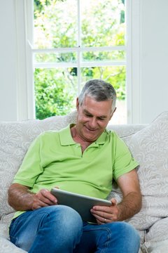Happy senior man with digital tablet in sitting room