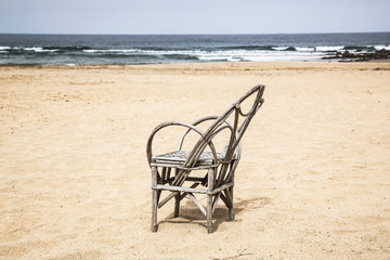 Fototapeta na wymiar silla de caña en una playa desierta con olas y cielo al fondo