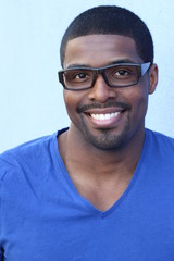 Close up Smiling Young Black Man Wearing Eyeglasses, Looking at the Camera Against Blue Wall Background 