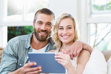 Portrait of couple sitting on sofa and using digital tablet
