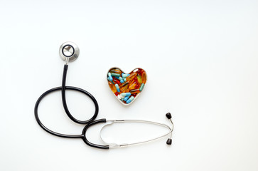 stethoscope on white background with pills in shape of heart