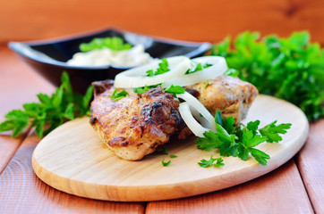 A piece of kebab on a wooden table with onion rings, white sauce and parsley