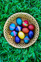 Easter eggs in the basket on the green grass. Top view