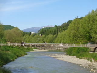 Подвесной мост через реку, деревья со свежей зеленой листвой, голубое небо