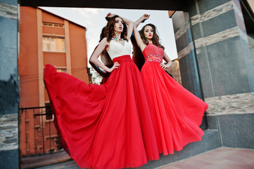 Two fashionable girls at red evening blowing dress in the air po