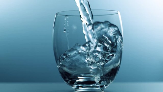 Wasser wird in Glas gesch&uuml;ttet, Zeitlupe, blauer Hintergrund
