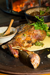 Delicious free range roasted goat shoulder served on a rustic metal plate by a hot open coal fire. Served with fresh parsley.