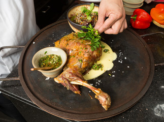 Delicious free range roasted goat shoulder served on a rustic metal plate by a hot open coal fire. Served with fresh parsley.