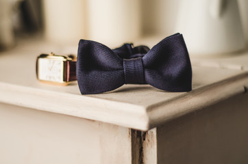 Classic groom accessories: blue bow tie and watch on a wooden table. Set of men's stylish vintage clothing. Male decoration for couple. Jewelry man. Groom's morning.