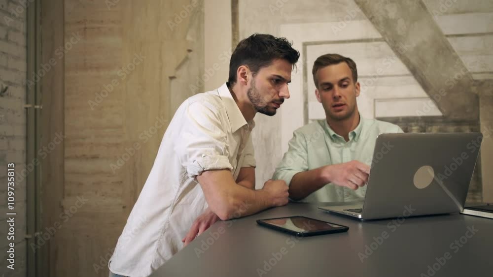Aufkleber one man sits by the big grey table. another male comes to the working place. businessmans work with 