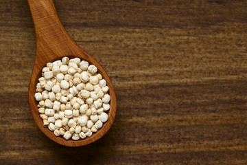 Gepuffte weisse Quinoa Samen (lat. Chenopodium quinoa) auf kleinem Holzlöffel, fotografiert mit natürlichem Licht