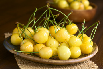 Reife gelbe Süsskirschen auf Teller, fotografiert auf dunklem Holz mit natürlichem Licht (Selektiver Fokus, Fokus auf die oberen Kirschen vorne)