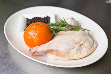 Free range raw duck leg, with herbs, orange and garlic, on a white plate. Duck wellington step by step.