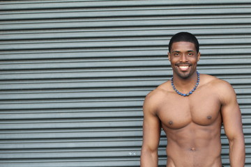 Obraz premium Under the sunshine, a masculine black guy, half naked, is standing with smiley expression / Portrait of Young Black Fitness Guy with copy space 