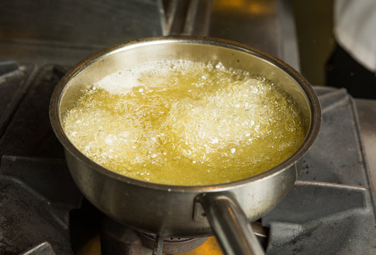 A pan of hot bubbling boiling oil in a silver pan on a hob.