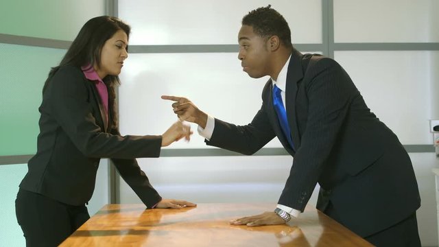 A businessman and businesswoman across a conference table from each other engage in a heated argument.