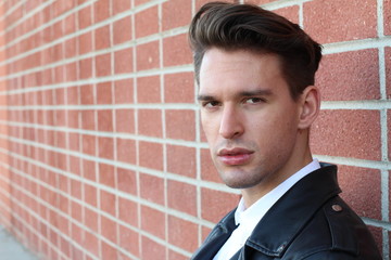 Fashion young man in white shirt and black leather jacket over modern blurred brick wall with copy space 