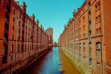 Naklejka premium Large river canal with bricks buildings on the sides, sun and shadow, color mix