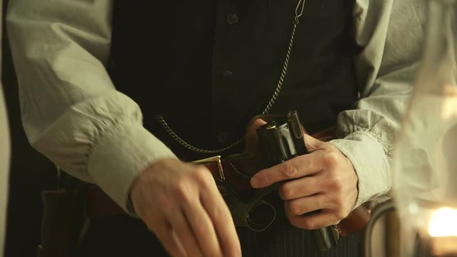 Bullets being loaded into an 1860 army pistol by a gunslinger or frontiersman from the American wild west era wearing a cross draw holster.