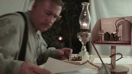 A telegrapher from the early American west era enters a tent he has made into a makeshift telegraph station and starts to work.