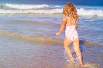 Fototapeta premium little girl run play with waves on the beach