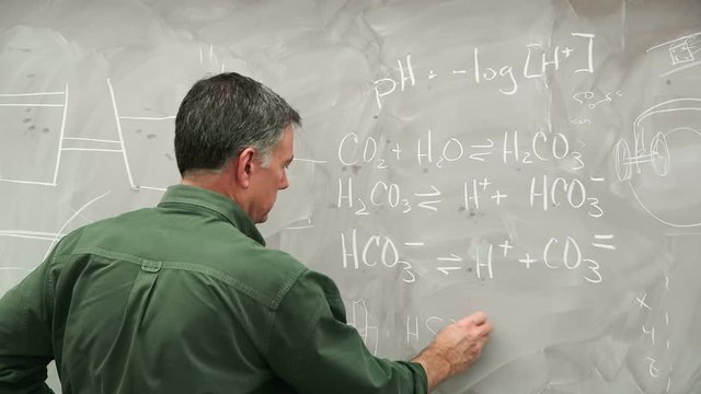 A chemist or chemistry teacher writing equations on a classic chalk filled chalkboard.