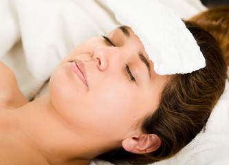 Obraz na płótnie Canvas Closeup headshot young woman lying down with eyes closed, white towel pad resting on forehead