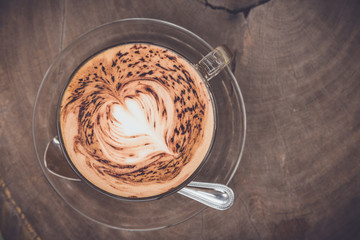 A cup of coffee with heart pattern on wooden background.Toned image.