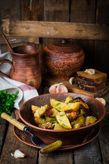 Roasted potatoes with garlic and fennel in clay bowl on wooden background. Selective focus