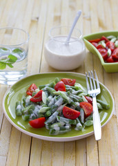 Salad of green beans and cherry tomatoes with yoghurt sauce on a yellow wooden background
