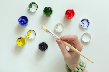Hand of Artist holding Brush and color Paints on white Table
