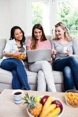 Beautiful female friends looking in laptop at home
