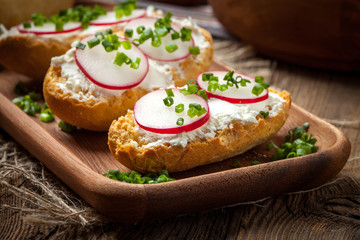 Toasts with radish, chives and cottage cheese on a wooden table.