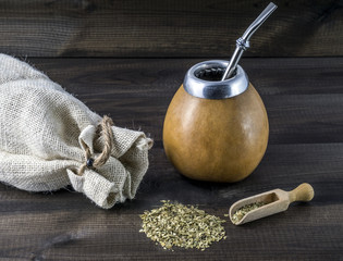 yerba mate with gourd matero, bombila, wooden spoon and linen bag on wooden background.