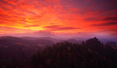 Fototapeta na wymiar Cold misty morning sunrise in a fall valley of Bohemian Switzerland park. Hill with view hut on hill increased from magical darkness with bloody sky, Mariina vyhlidka, Ceske Svycarsko, Czech Republic