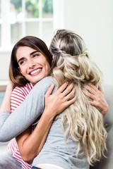 Close-up of happy beautiful woman hugging female friend on sofa at home