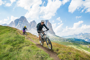A man and a woman on  mountain bikes racing along trail in the Dolomites,  Val Gardena, Italy
