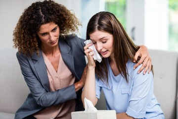 Close-up of female psychologist consoling depressed woman on sofa at home