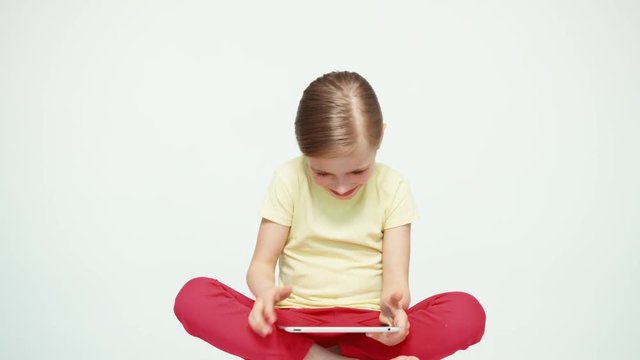Girl 7-8 years old using tablet pc and laughing and sitting on the white background