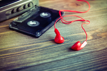 Audio cassette tapes and red earphones and player over wooden table, vintage style, selective focus