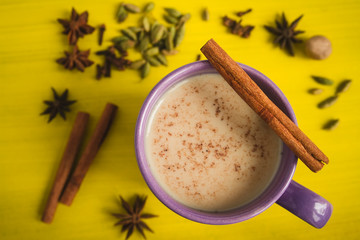 Traditional milk tea with spices on a yellow table