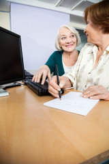 Senior Woman Using Computer While Classmate Writing Notes