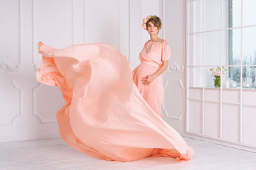 Pregnant woman dancing in pink evening dress flying on wind. Waving fabric, fashion shot.