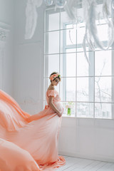 Naklejka premium Pregnant woman dancing in pink evening dress flying on wind. Waving fabric, fashion shot.