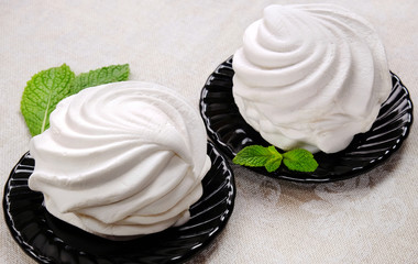 White sweet marshmallow dessert on black saucers with sprigs of fresh mint on linen fabric.