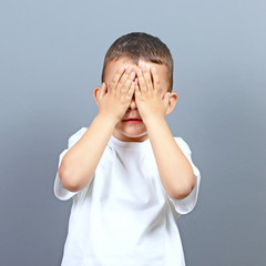 Cute little boy kid covering his face with hands against gray ba