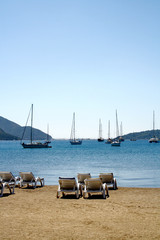 Sun bed on a beach and a yacht. Canvas Chair on tropical beach